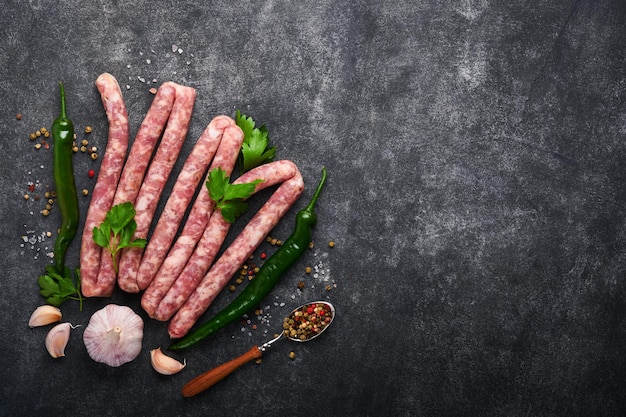 Rohwürste Bratwurst oder Würstchen mit Zutaten auf einem Schneidebrett mit Gewürzen auf einem Steinhintergrund mit Kopierbereich Hintergrund zum Kochen von Speisen Ansicht von oben