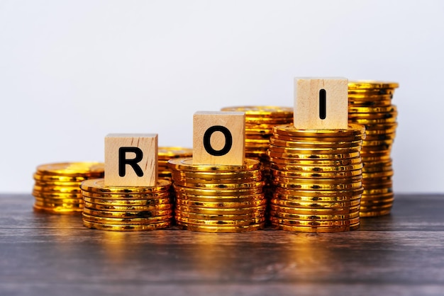 ROI Return of Investment Text auf Holzblock mit Stapel Münzen