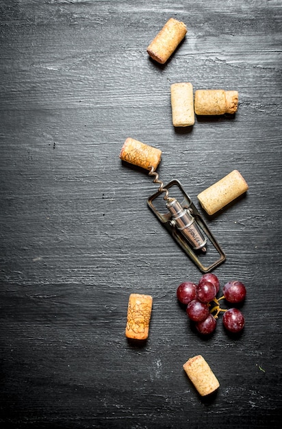 Rolhas de vinho com saca-rolhas e ramo de uva na mesa de madeira preta.