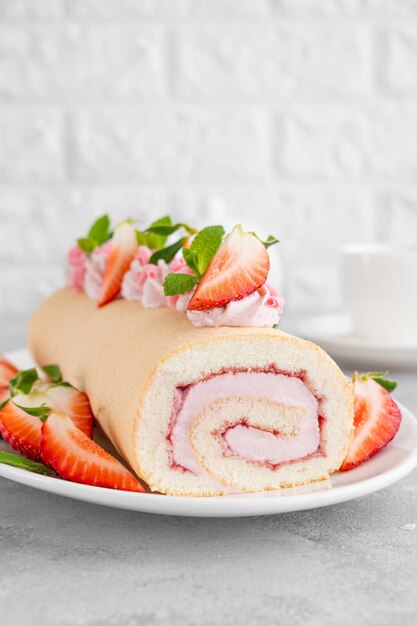 Rolinho de bolo com geléia de morangos frescos e cream cheese em um prato branco sobre um fundo cinza