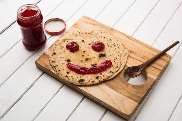 Rolinho de Chapati com Ketchup de Tomate ou Geléia de Geléia de Fruta com rosto sorridente, cardápio de comida favorita de crianças indianas para caixa de tiffin escolar, foco seletivo