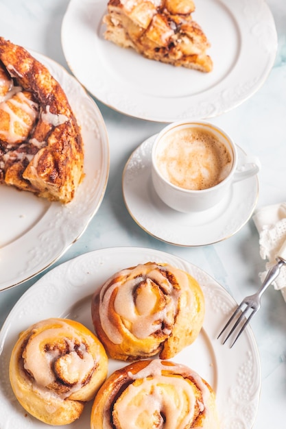 Rolinhos de canela caseiros em um prato branco sobre uma mesa branca com café e pães de pastelaria no café da manhã