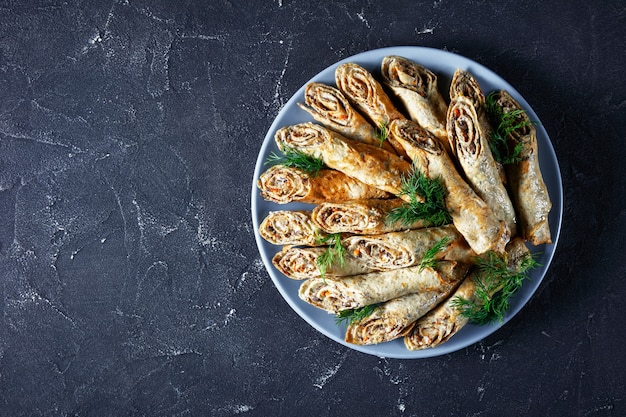 Rolinhos de crepe de trigo sarraceno com carne, vegetais e cogumelos em um prato sobre uma mesa de concreto, vista de cima, camada plana