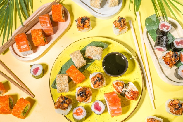 Rolinhos de sushi com arroz e peixe, molho de soja e pauzinhos na superfície amarela, flatlay moderno à luz do dia