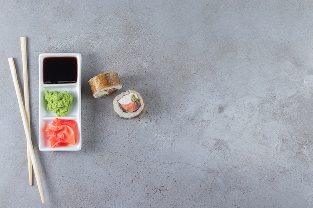 Rolinhos de sushi com molho de soja colocados em um quadro branco com pauzinhos.
