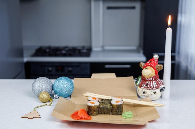 Rolinhos japoneses com peixe vermelho em uma caixa de papelão aberta sobre a mesa Decoração de mesa em estilo festivo Brinquedos de Natal e uma vela