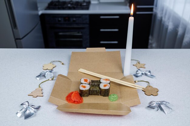 Rolinhos japoneses com peixe vermelho em uma caixa de papelão aberta sobre a mesa Decoração de mesa em estilo festivo Brinquedos de Natal e uma vela