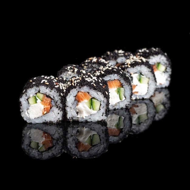 Roll Smoked California con pepino, aguacate, anguila y caviar tobiko negro sobre negro con reflejos. De cerca. Cocina japonesa. Foto para el menú