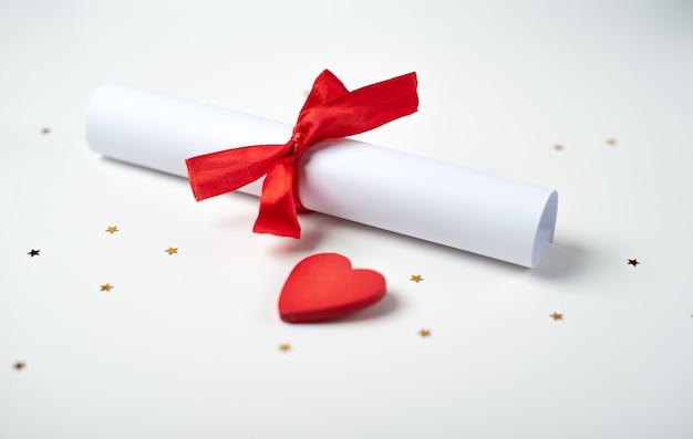 Rolled Valentinstag Liebesbrief mit einem roten Band und rotem Holzherz auf dem hellen (weißen) Hintergrund gebunden