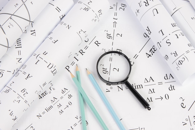 Rollen von Papierzeichnungen mit mathematischen elektrischen Formeln, Lupe und Bleistiften