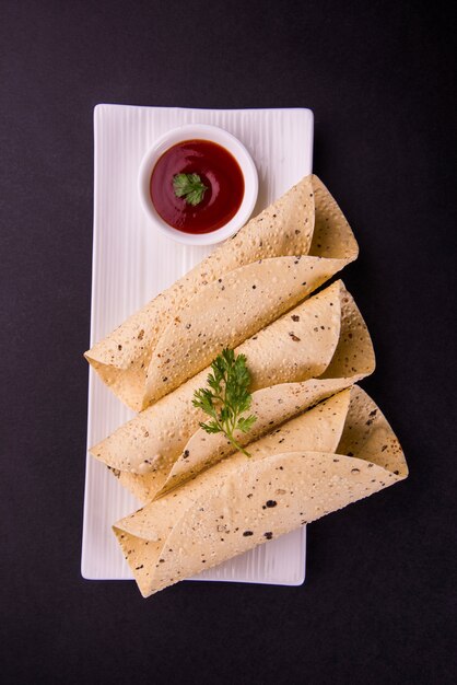 El rollito de papad asado es una comida o guarnición tradicional de la India que se sirve con salsa de tomate sobre una mesa colorida o de madera. Enfoque selectivo