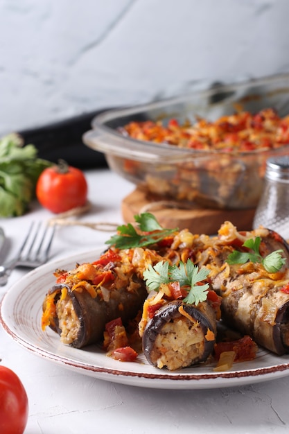 Rollitos de berenjena al horno con pollo, cebolla y zanahoria en placa en gris.