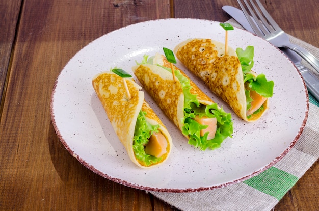 Rollitos de bocadillos de panqueques, salmón y hojas de ensalada verde.