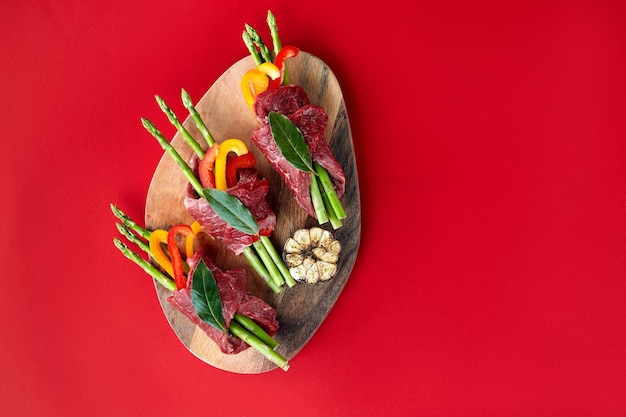 Rollitos de carne cruda y guarniciones de verduras frescas listas para cocinar sobre un fondo blanco