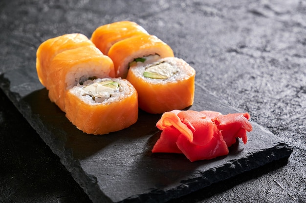 Rollitos de Filadelfia con salmón pescado aguacate queso crema jengibre en placa de piedra sobre fondo oscuro