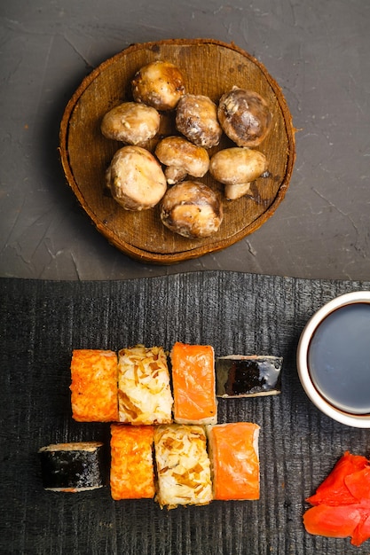 Rollitos con pescado y gambas en una pizarra negra junto a palitos de salsa de soja y champiñones al horno