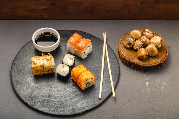 Rollitos con pescado y gambas en una tabla redonda junto a palitos de salsa de soja y champiñones al horno