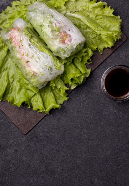 Rollitos de primavera con plato verde junto a una salsa gris sobre negro.