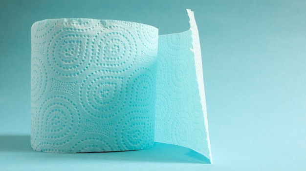 Rollo azul de papel higiénico moderno sobre un fondo azul. Producto de papel en una funda de cartón, utilizado con fines sanitarios a partir de celulosa con recortes para facilitar el desgarro. Dibujo en relieve. Copie el espacio.