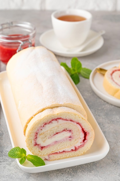 Rollo de bizcocho con mermelada de fresa y crema en un plato blanco sobre un fondo gris Copiar espacio