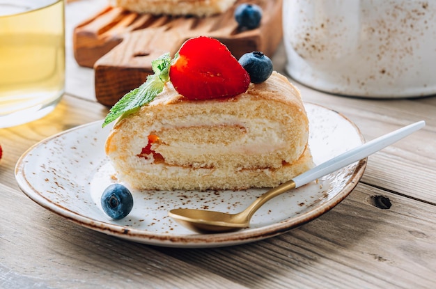 Rollo de bizcocho relleno de nata montada decorado con flores de fresa, arándanos, menta y jazmín