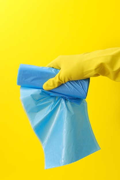 Rollo de bolsas de basura en mano con guante sobre fondo amarillo