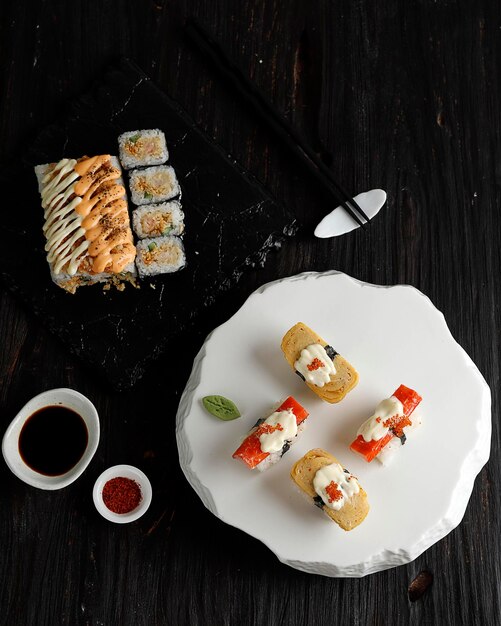 Rollo de california de cocina japonesa y rollo de atún en una tabla de madera negra servido con wasabi y salsa de soja