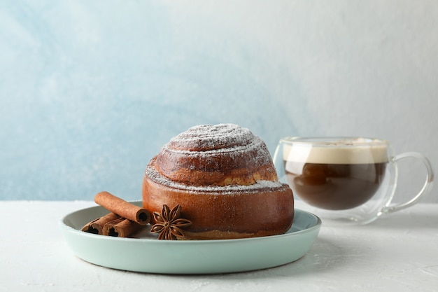 Rollo de canela, anís y una taza de capuchino con caramelo en la mesa blanca