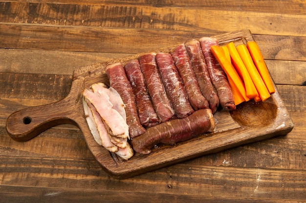 Rollo de carne cruda para preparar con tocino y zanahorias en una tabla de cocina