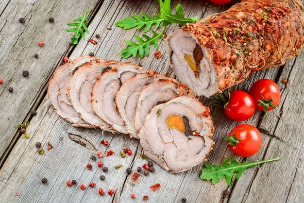 Rollo de cerdo asado relleno de albaricoques secos, queso y nueces, sobre una mesa de madera