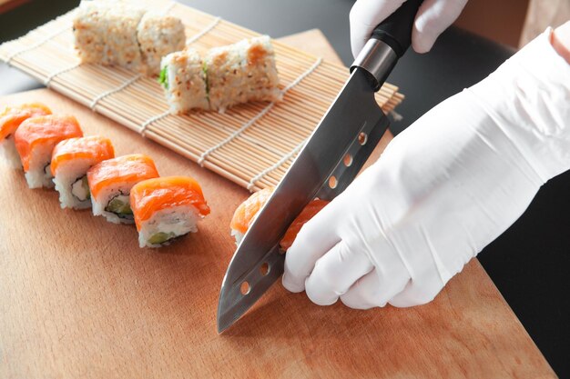 Rollo Filadelfia cortado con un cuchillo sobre una tabla de madera Un hombre con guantes Cocina segura