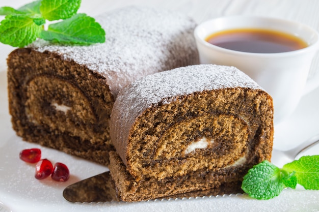 Rollo de la galleta del chocolate y una taza de té en la tabla de madera blanca.