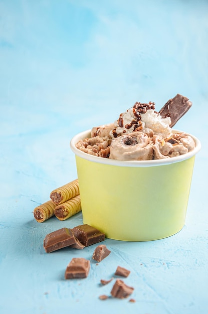 Rollo de helado de chocolate y café, con trozos de chocolate y galletas sobre fondo azul.