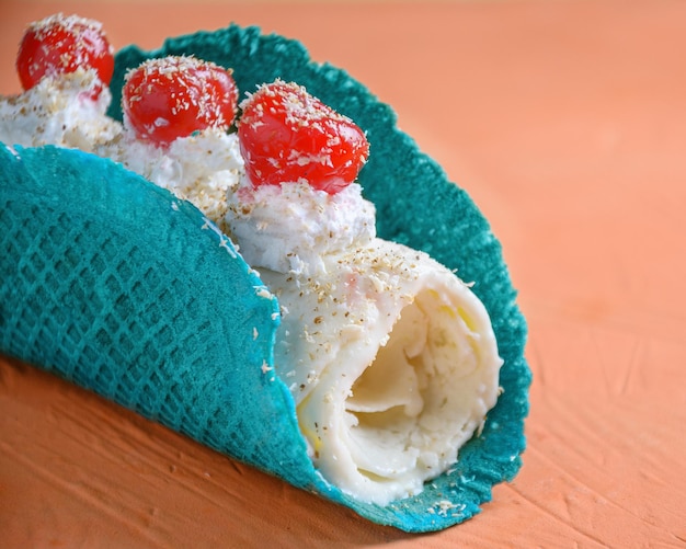 Rollo de helado de piña colada en cono de galleta y cerezas sobre fondo naranja