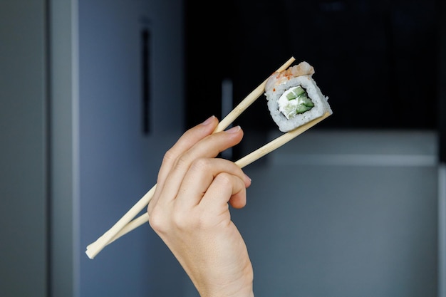 Rollo japonés Filadelfia La chica sostiene sushi con palillos Fondo borroso