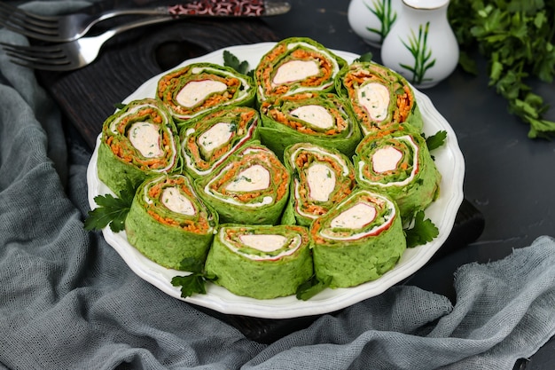 Rollo de lavash con palitos de cangrejo, espinacas, perejil y zanahorias al estilo coreano en un plato sobre un fondo oscuro