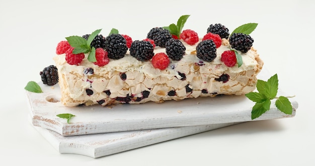 Rollo de merengue al horno con crema y frutas frescas sobre una tabla de madera blanca delicioso postre