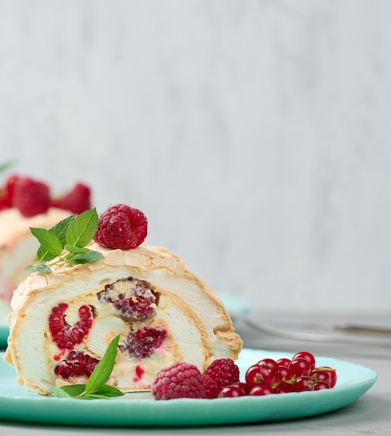 Rollo de merengue al horno con frutos rojos sobre un plato redondo de fondo blanco.