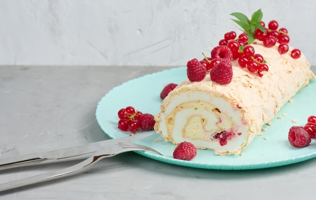 Rollo de merengue al horno con frutos rojos sobre un plato redondo de fondo blanco.