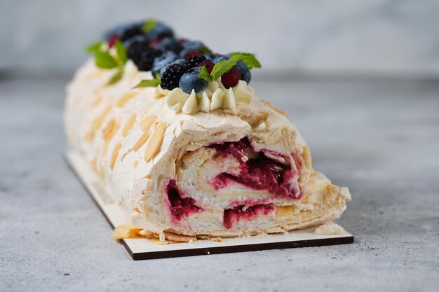 Rollo de merengue con crema de queso crema, aderezado con frutos rojos frescos.