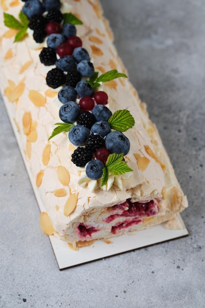 Rollo de merengue con crema de queso crema, aderezado con frutos rojos frescos.