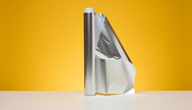 Rollo de papel de aluminio retorcido para envasar alimentos sobre fondo amarillo