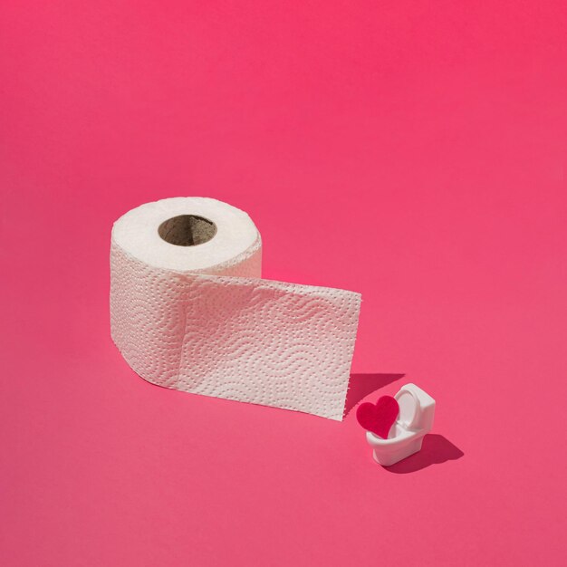 Foto rollo de papel higiénico pequeño inodoro con corazón de felpa sobre fondo rosa concepto mínimo