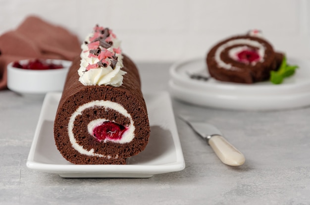 Rollo de pastel de chocolate de la selva negra con crema batida y relleno de cereza sobre un fondo gris. Copie el espacio.