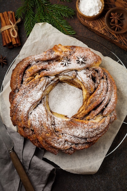 Rollo de pastel de Navidad con canela y azúcar en polvo sobre un fondo de piedra o hormigón antiguo oscuro