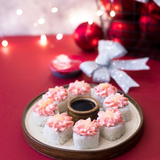 Rollo de queso crema en rojo con guirnaldas de luces. Rollos de sushi cubiertos con crema rosada y camarones