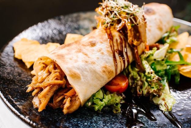 Rollo relleno de carne de cerdo desmenuzada con ensalada verde y patatas fritas sobre fondo oscuro