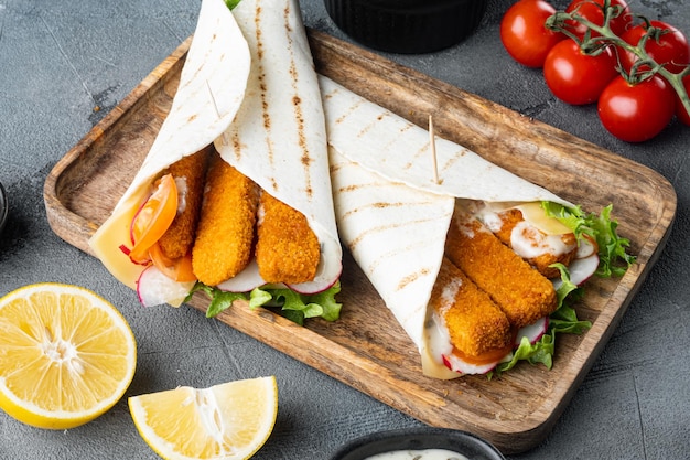 Rollo de sándwich con palitos de pescado, queso y verduras, en bandeja de madera, sobre fondo gris