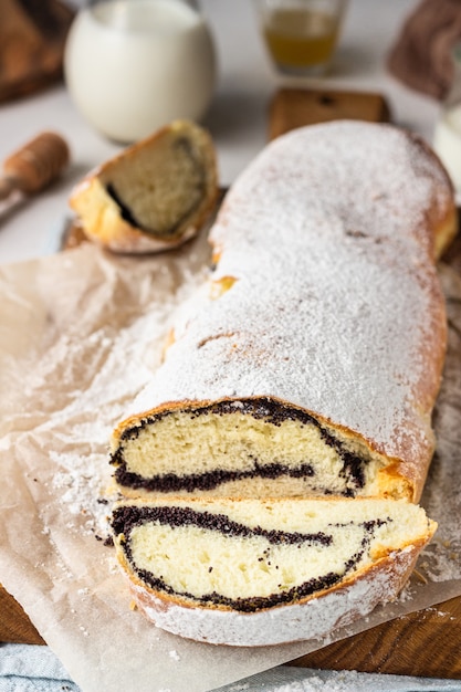 Rollo de semillas de amapola o strudel sobre tabla de madera espolvoreado con azúcar en polvo.