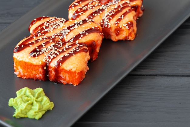 Foto rollo de sushi al horno servido en placa negra sobre mesa de madera cerrar